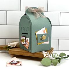 a green mailbox sitting on top of a wooden board next to flowers and cards