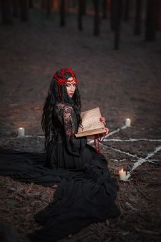 a woman sitting on the ground holding an open book in her hands with candles around her