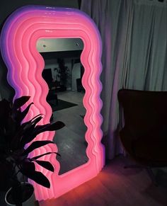 a large pink mirror sitting on top of a wooden floor next to a chair and potted plant