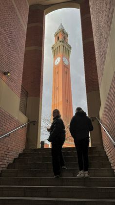 two people are standing on the stairs in front of a tower with a clock at the top