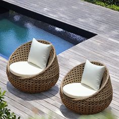 two wicker chairs sitting on top of a wooden deck next to a swimming pool