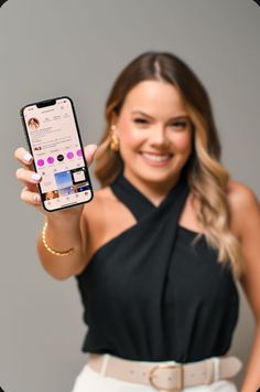 a woman holding up a cell phone in her right hand and smiling at the camera