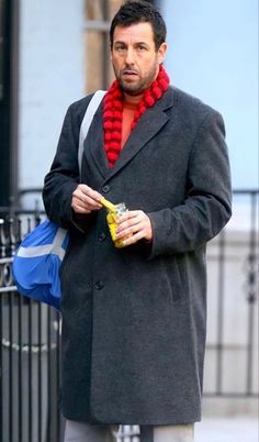 a man with a red scarf on his neck is walking down the street while holding a drink