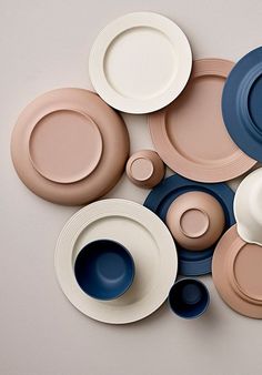 many different colored plates and bowls on a white table top, with one empty plate in the middle