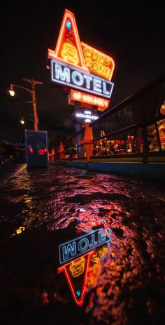 the neon signs are reflected in the wet surface of the water that is running through the street