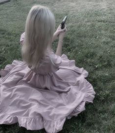 a woman sitting on the ground holding a cell phone in her hand and wearing a pink dress