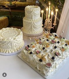 two wedding cakes sitting on top of a table next to each other with candles in the background