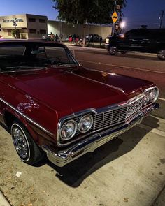 an old red car is parked on the side of the road