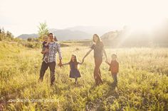 a family holding hands and walking through the grass with mountains in the background at sunset