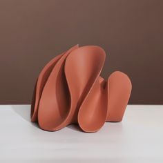 an orange sculpture sitting on top of a white table next to a brown wall in the background