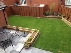 a small backyard with grass and wooden fenced in areas for seating, table and chairs