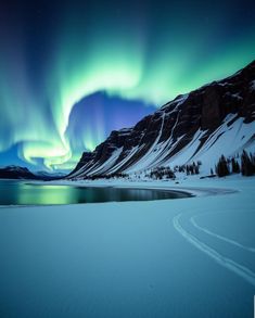 an aurora bore is seen above the snow covered mountains and lake in this winter scene