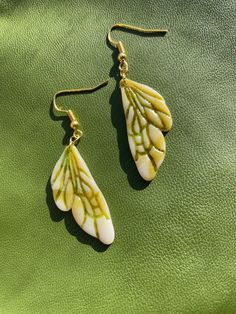 two white and green leaf shaped earrings sitting on top of a green leather surface next to each other