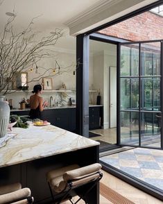 a woman standing at the kitchen counter in front of an open glass door that leads to another room