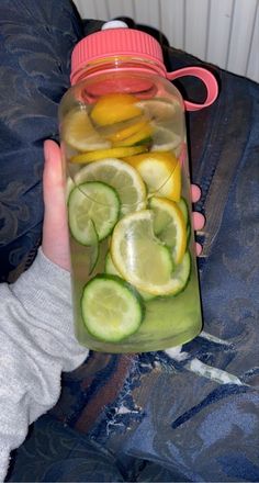 a person holding a mason jar filled with sliced lemons, cucumbers and water