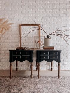 two black tables sitting next to each other in front of a white brick wall with dried flowers on top