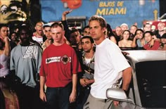 a group of young men standing next to each other in front of a white car