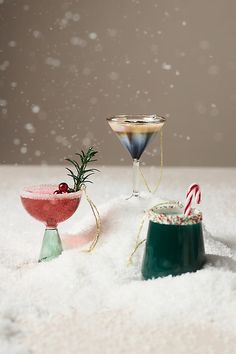 two martini glasses with candy canes in them on top of snow covered ground next to each other