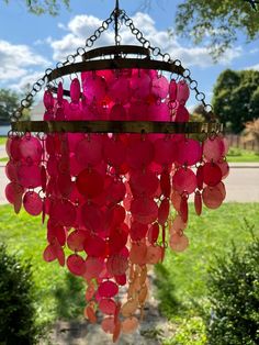 a pink chandelier hanging from a tree in front of a green field and blue sky