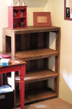 a red table with some books on top of it next to a book case and shelf