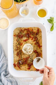 someone is adding seasoning to a dish in a white casserole pan on a marble countertop