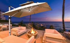 an outdoor fire pit with chairs and umbrellas on the deck overlooking the ocean at dusk