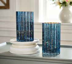 two blue glass vases sitting on top of a white table next to each other