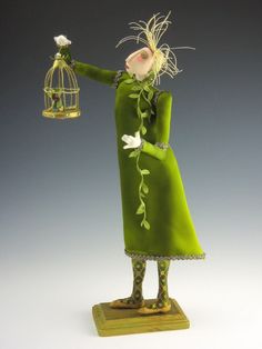 a green figurine holding a bird cage with flowers in it's beak