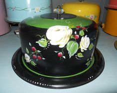 a black and green cake with white flowers on it sitting on a table next to other cakes