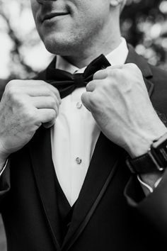 a man in a tuxedo adjusts his bow tie