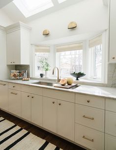 a kitchen with white cabinets and an area rug in front of the window that has light coming through