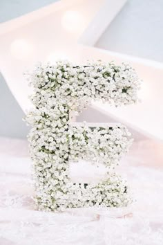 the letter e is made up of small white baby's breath flowers and sits on a table