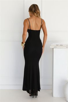 the back of a woman in a black dress standing next to a white table and wall