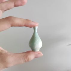 a hand holding a small green vase in it's left hand, against a white background