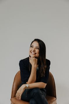 a woman sitting in a chair with her hand on her chin and smiling at the camera