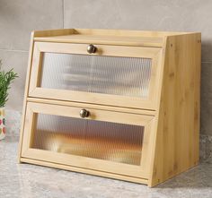 a wooden cabinet with two glass doors on the top and bottom, next to a potted plant