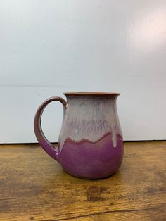 a purple and white mug sitting on top of a wooden table next to a wall