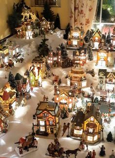 a christmas village is shown in front of a window with snow on the ground and lit up buildings