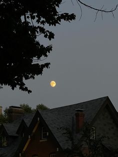 a full moon is seen over a house in the evening sky with trees around it