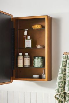 a wooden medicine cabinet with bottles and soaps on the top shelf next to a towel