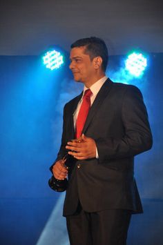 a man in a suit and red tie standing on stage with his hands clasped to his chest