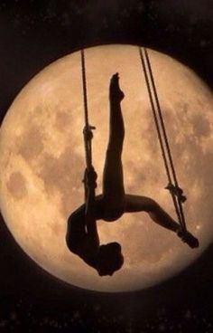 a man hanging upside down on a rope in front of the moon