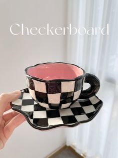 a hand holding a black and white checkerboard coffee cup on a saucer