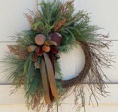 a wreath with pine cones and other decorations hanging on a door