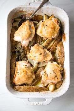 a casserole dish filled with chicken and potatoes, garnished with herbs