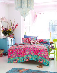 a bed room with a neatly made bed next to a dresser and window filled with flowers