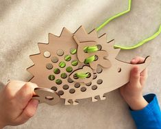 a child's hands holding a wooden hedgehog clock with green dots on it