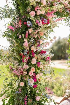 an arrangement of flowers is hanging from the side of a wooden structure with greenery