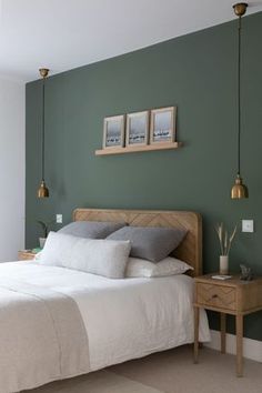 a bedroom with green walls and white bedding, two framed pictures on the wall