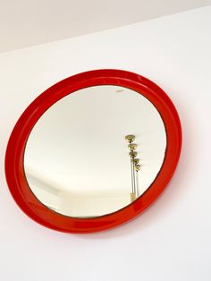 a red round mirror hanging on the wall next to a white wall with a lamp